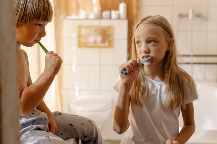 dwoje dzieci myje zęby szczoteczkami do zębów