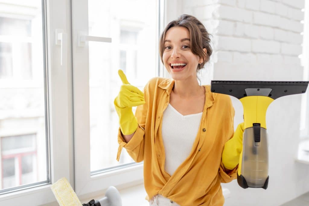 Kobieta w rękawiczkach zadowolona z trzymanej w dłoni akumulatorowej myjki do okien