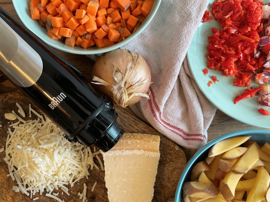 Blender Braun w otoczeniu składników: marchewki pokrojonej w kostkę, frytek, tartego sera oraz siekanych warzyw
