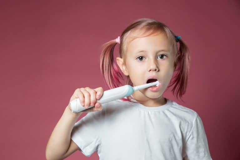 Dziewczynka z kucykami czyszcząca zęby białą szczoteczką elektryczną dla dzieci