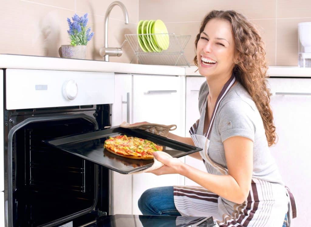 Uśmiechnięta kobieta wyjmuje blachę z pizzą z piekarnika parowego do zabudowy