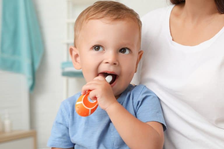 Małe dziecko ze szczoteczką do zębów 0-3 w ustach siedzące na kolanach rodzica