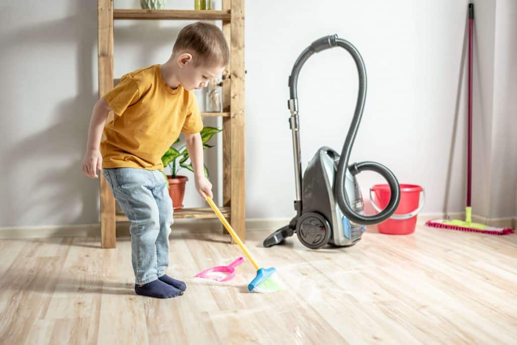 Mały chłopczyk pomaga sprzątać swój pokój a w tle stoi odkurzacz i mop