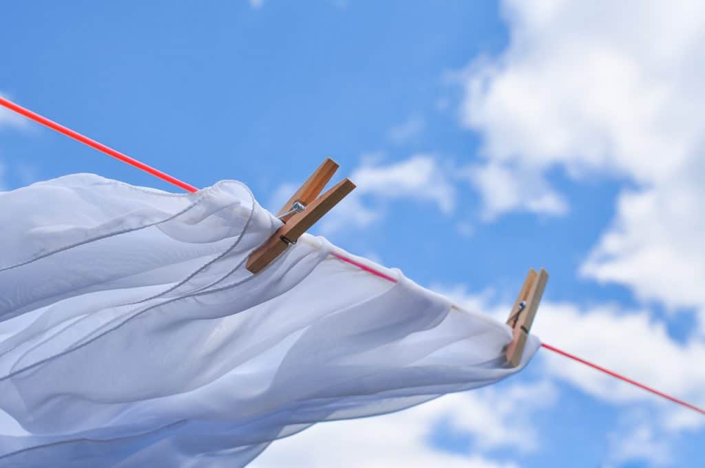 Biała koszula wietrzy się rozwieszona na lince do prania i przypięta spinaczami