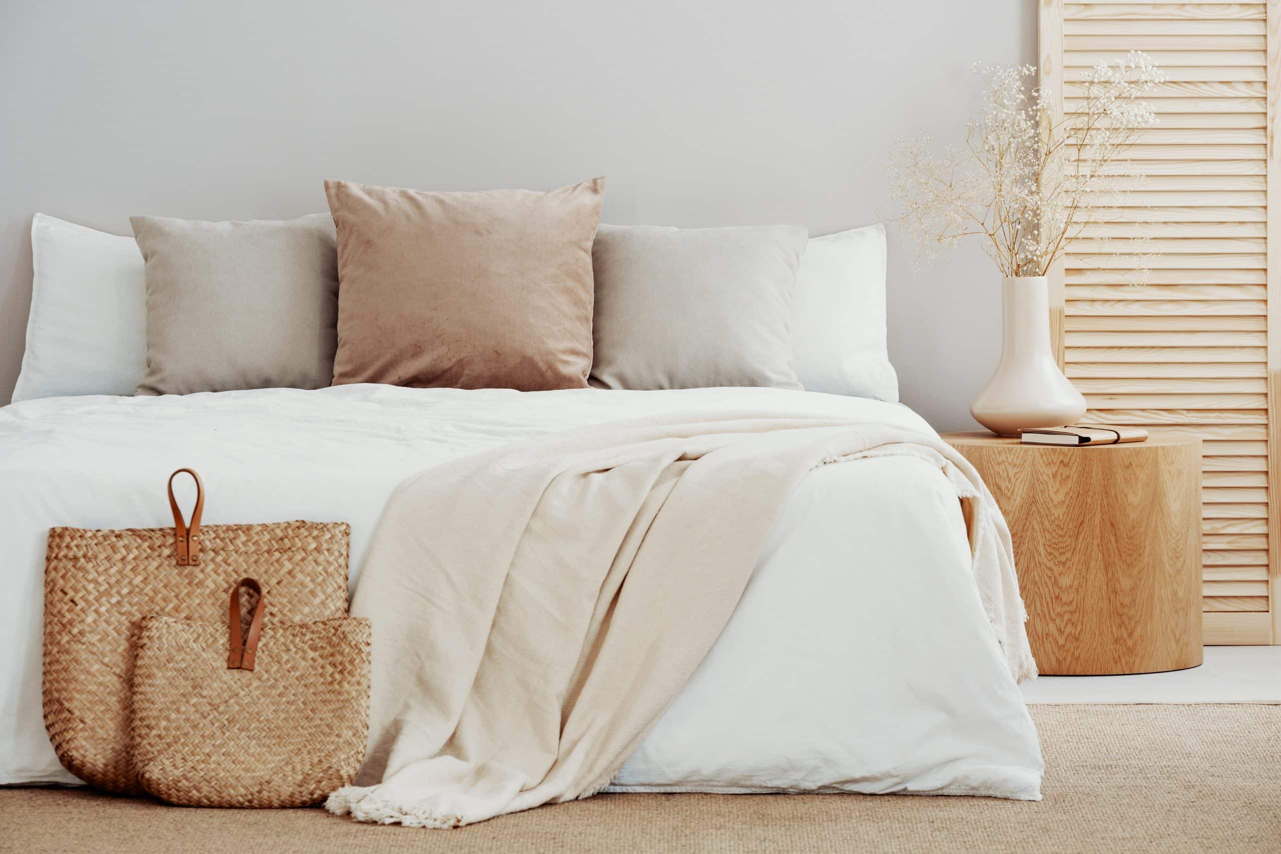 Łóżko z białą pościelą hotelową i beżowymi poduszkami; obok naturalne dekoracje