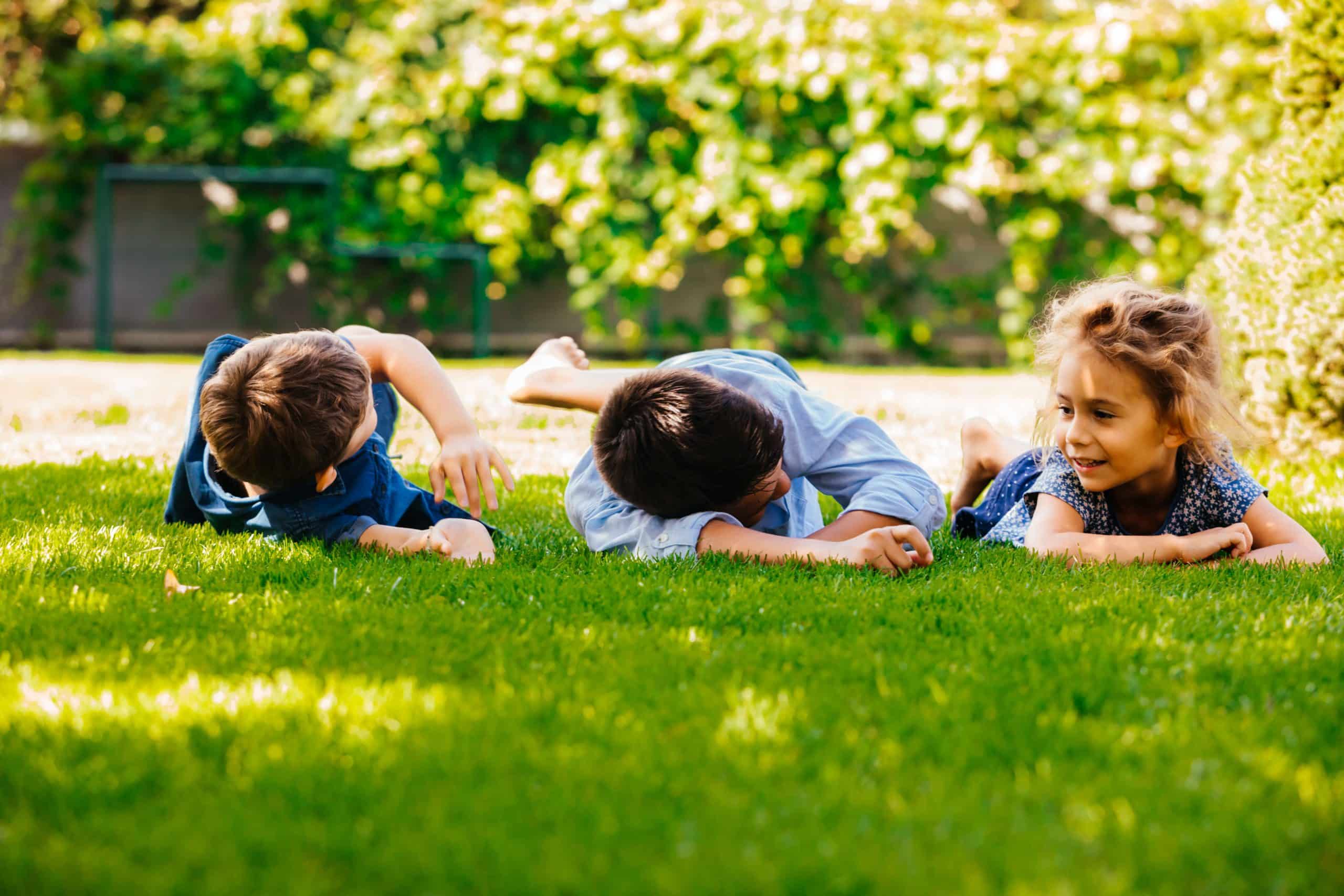 Troje dzieci odpoczywa na zielonej trawie w ogrodzie w wiosenny dzień