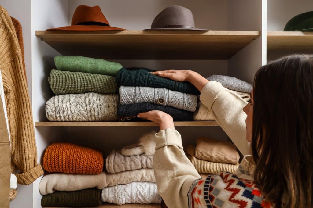 Kobieta wyjmuje poskładane swetry z szafy, by pozbyć się zapachu stęchlizny i wilgoci z tych ubrań