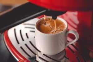 Czarna kawa w białej filiżance przygotowana z pomocą czerwonego ekspresu do espresso