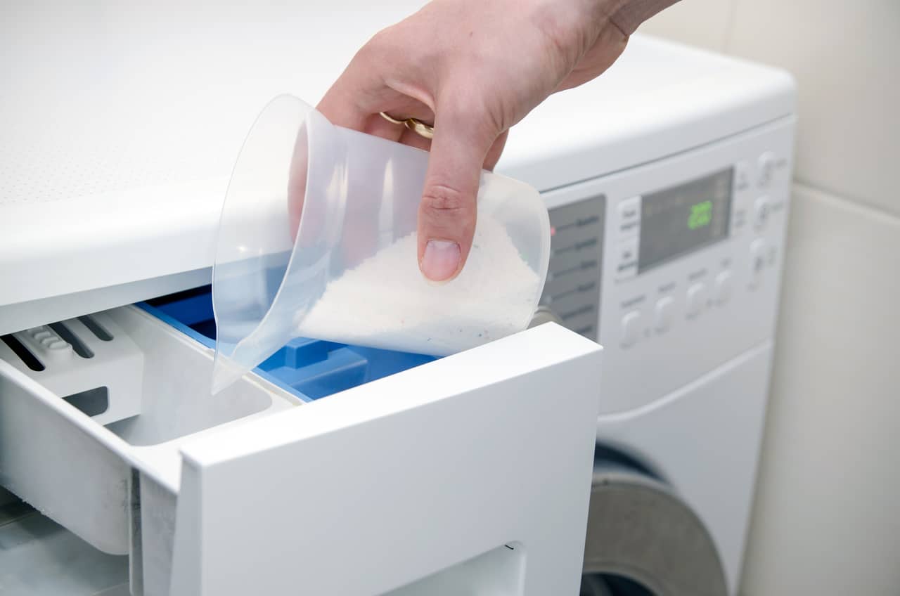 Męska dłoń wsypująca proszek do dozwownika na detergent w pralce