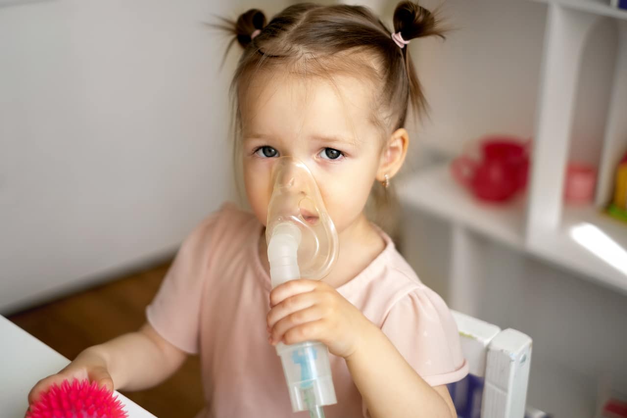 Mała dziewczynka z inhalatorem przy buzi cierpiąca na katar i kaszel alergiczny spowodowany grzybem i wilgocią w domu