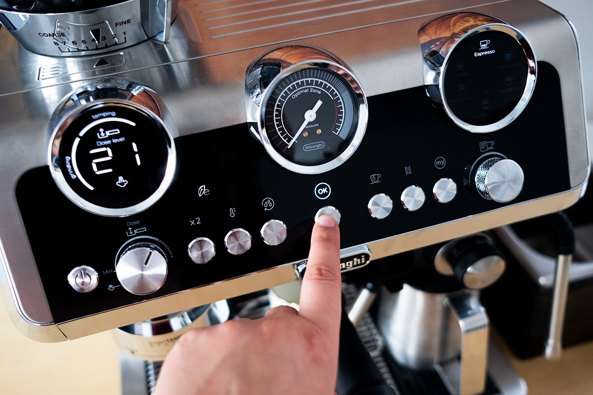 Dłoń naciskając przycisk na panelu sterowania ekspresu półautomatycznego De’Longhi La Specjalista Maestro