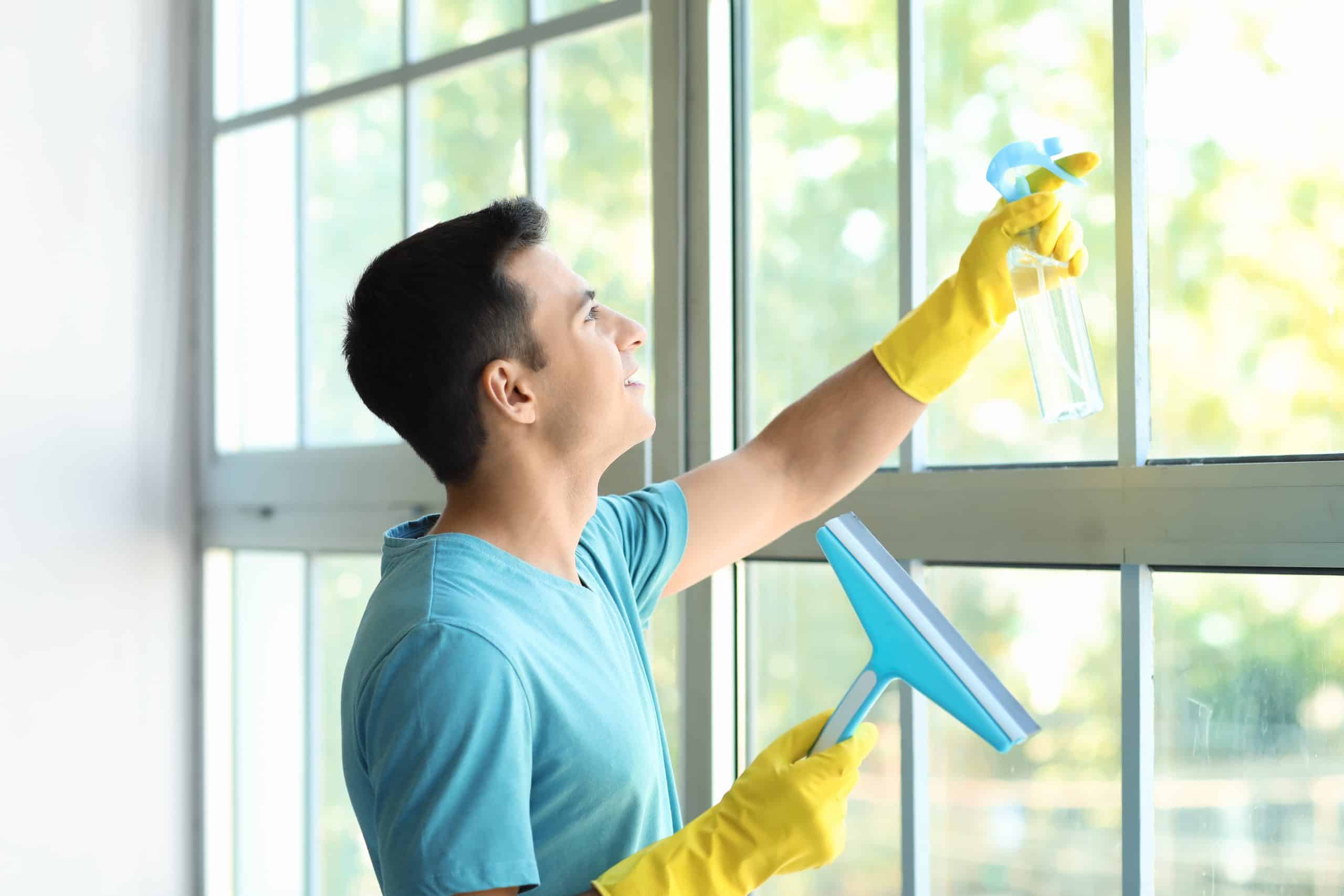 Mężczyzna ze ściągaczką do szyb i płynem w sprayu myje duże okna w domu