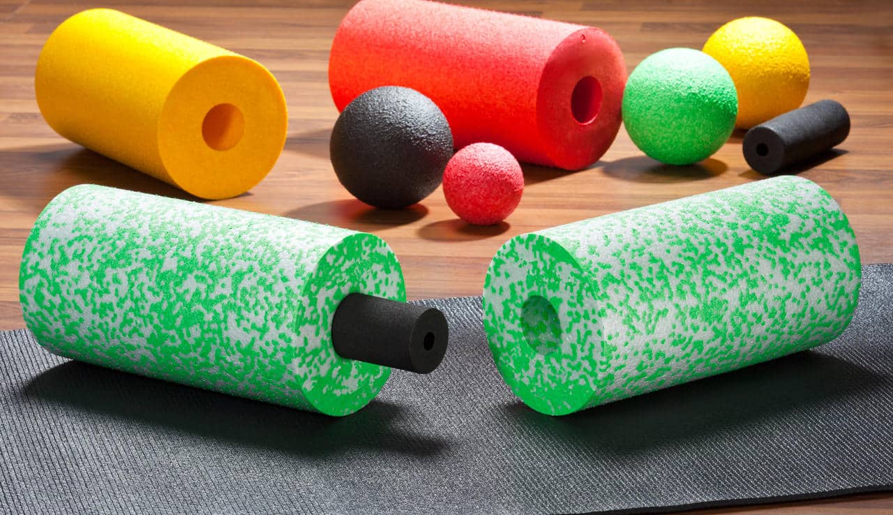 Rollery i piłki piankowe Blackroll w różnych kolorach leżące na podłodze i macie treningowej