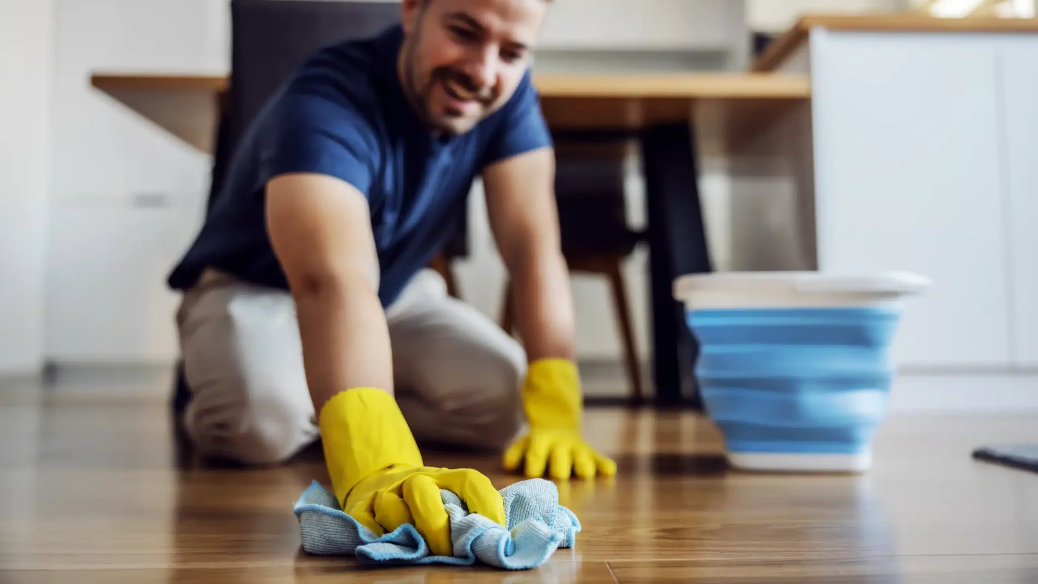 Mężczyzna w trakcie mycia podłogi po malowaniu, który klęczy na posadzce i myje ją wilgotną ściereczką