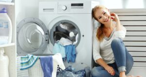 Młoda kobieta siedzi na podłodze obok dobrej pralki automatycznej wybranej z pomocą rankingu pralek
