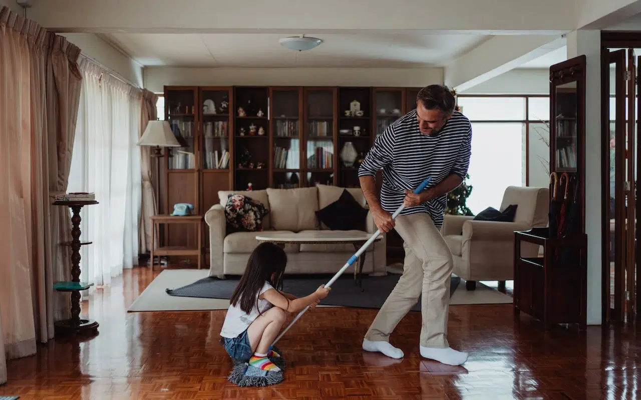 jciec i córka mopujący podłogę w klasycznym salonie - dziecko kuca na mopie i jest ciągnięte przez tatę. 
