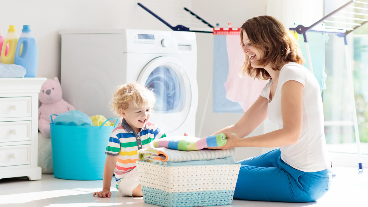 Kobieta i dziecko składają ręczniki wysuszone w suszarce tle pralnia i  trwający cykl suszenia ubrań w suszarce bębnowej