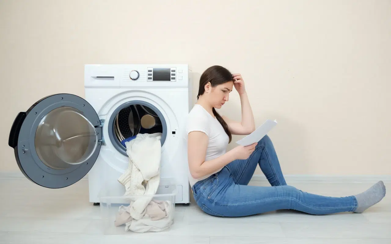 kobieta siedzi przy pralce i sprawdza w instrukcji, jak zresetować pralkę