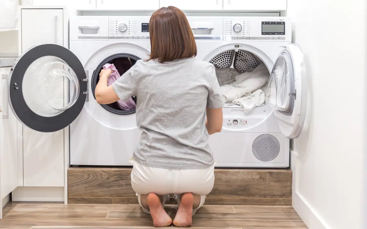 kobieta kuca przy pralce i wyjmuje z niej ubrania, żeby wykonać reset pralki