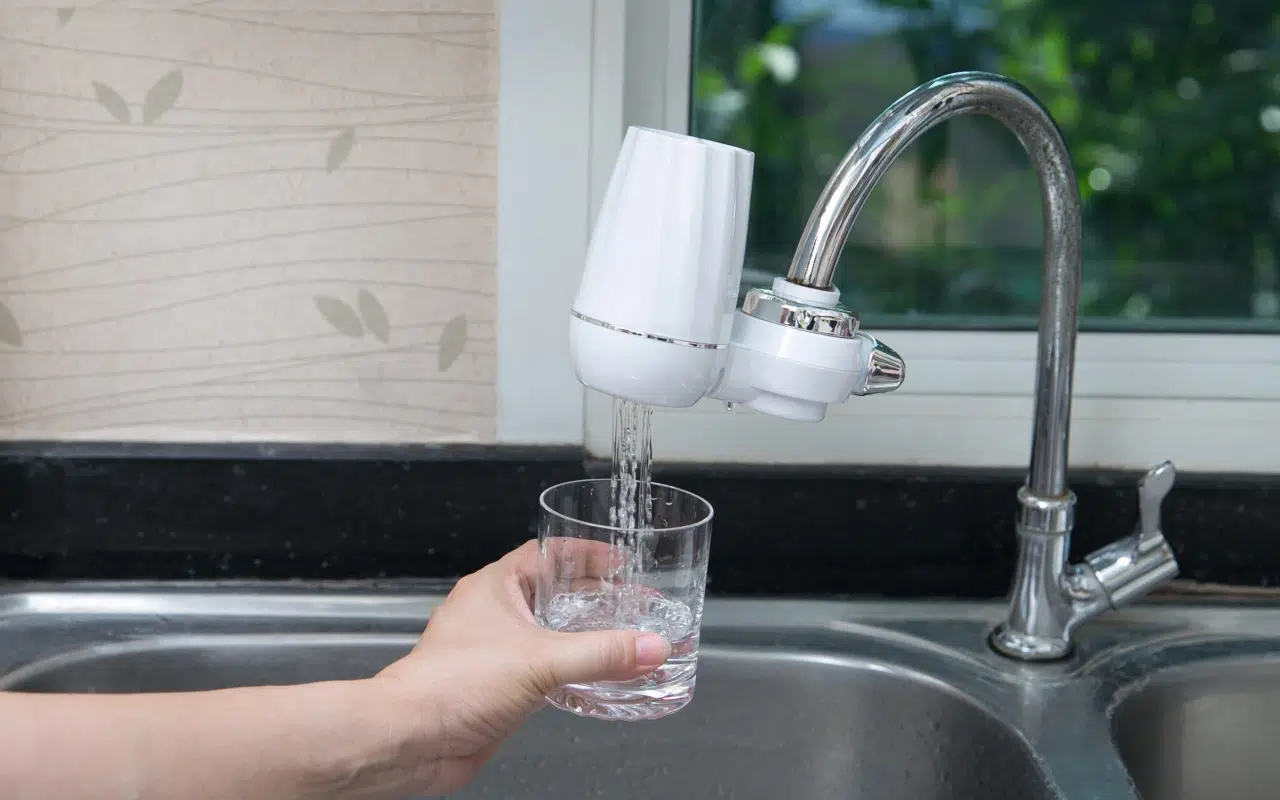 filtr wody na kran, z którego filtrowana woda leje się do podstawionej szklanki