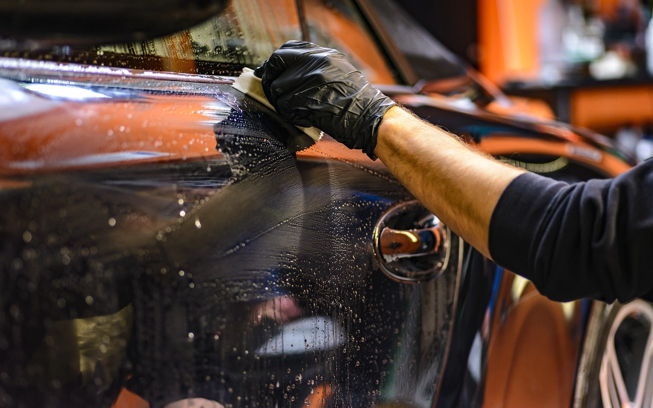 Męska dłoń w czarnych rękawiczkach myje karoserię czarnego samochodu.