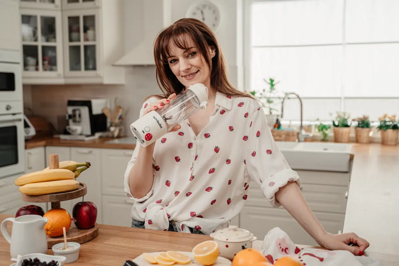 Uśmiechnięta kobieta trzyma w dłoni przenośny blender personalny nutribullet® Portable