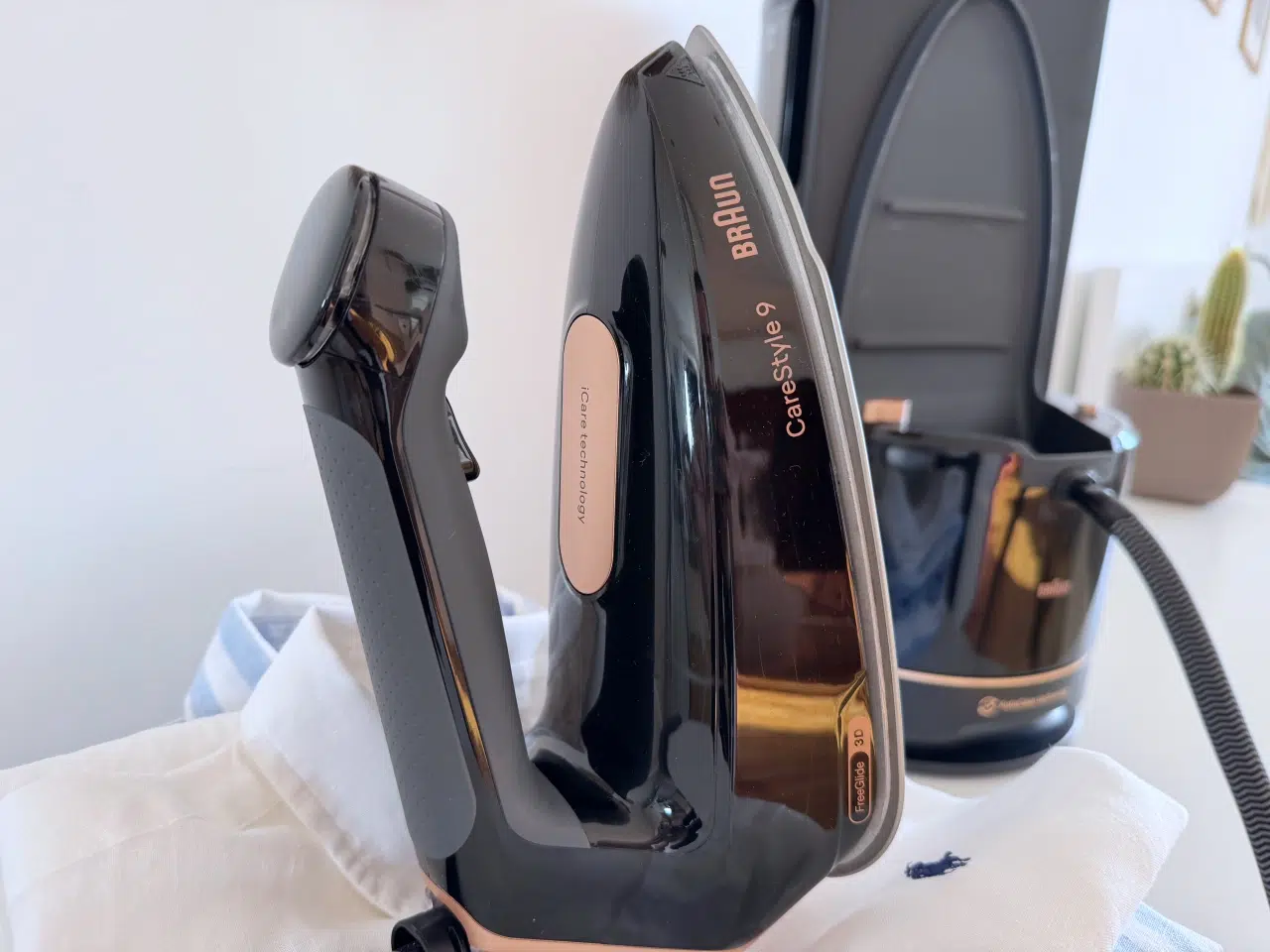 żelazko z generatorem pary Braun CareStyle 9 stoi na stosie wyprasowanych koszul