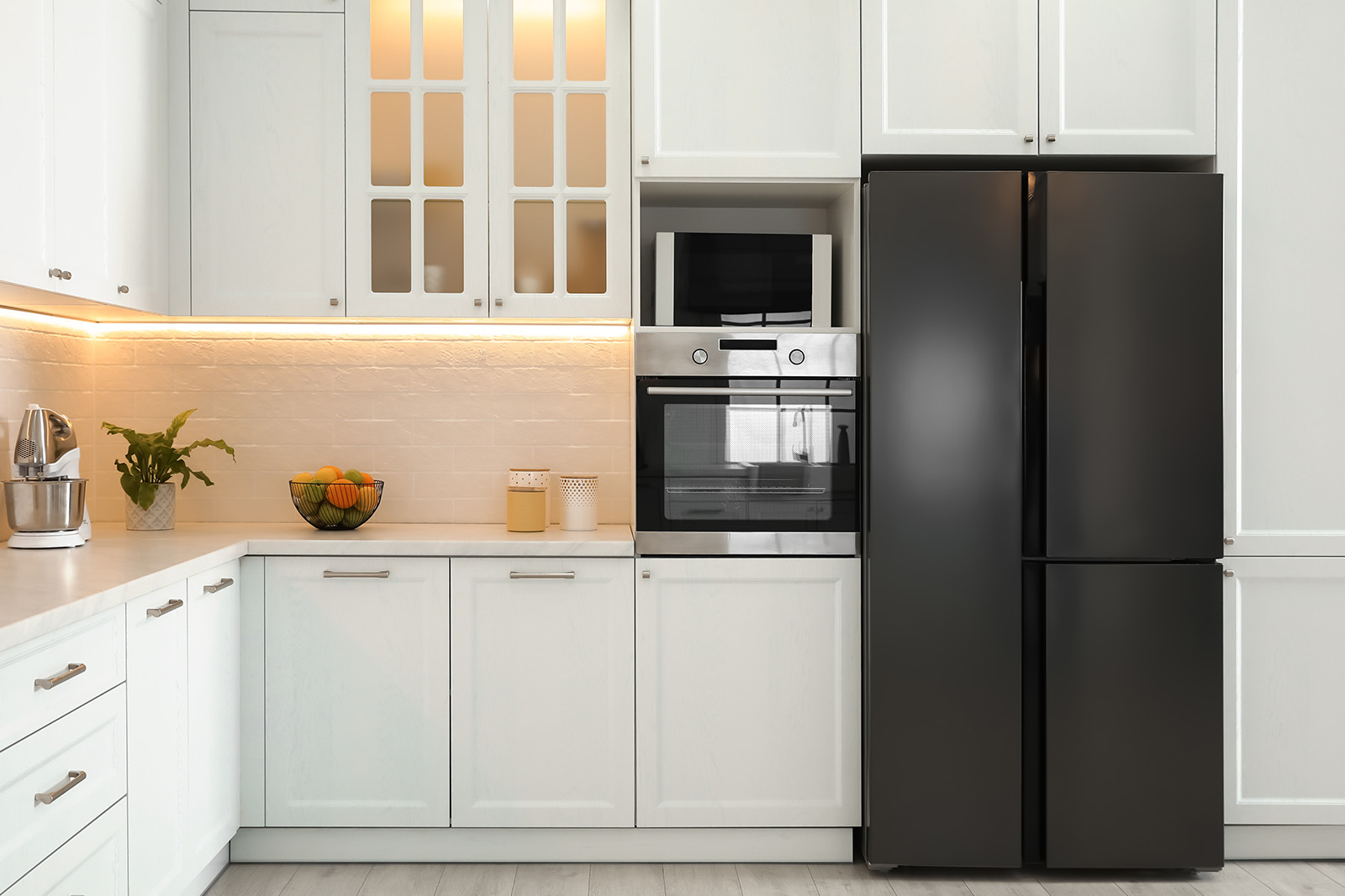 Nowoczesna kuchnia z białymi meblami, czarną lodówką i urządzeniami kuchennymi, w tym piekarnikiem i mikrofalówką. - tytułowa