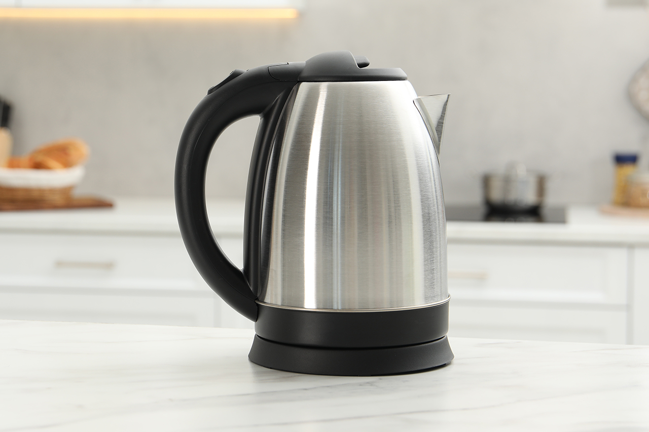 Stalowy czajnik elektryczny z czarnym uchwytem na tle nowoczesnej kuchni. - zdjęcie