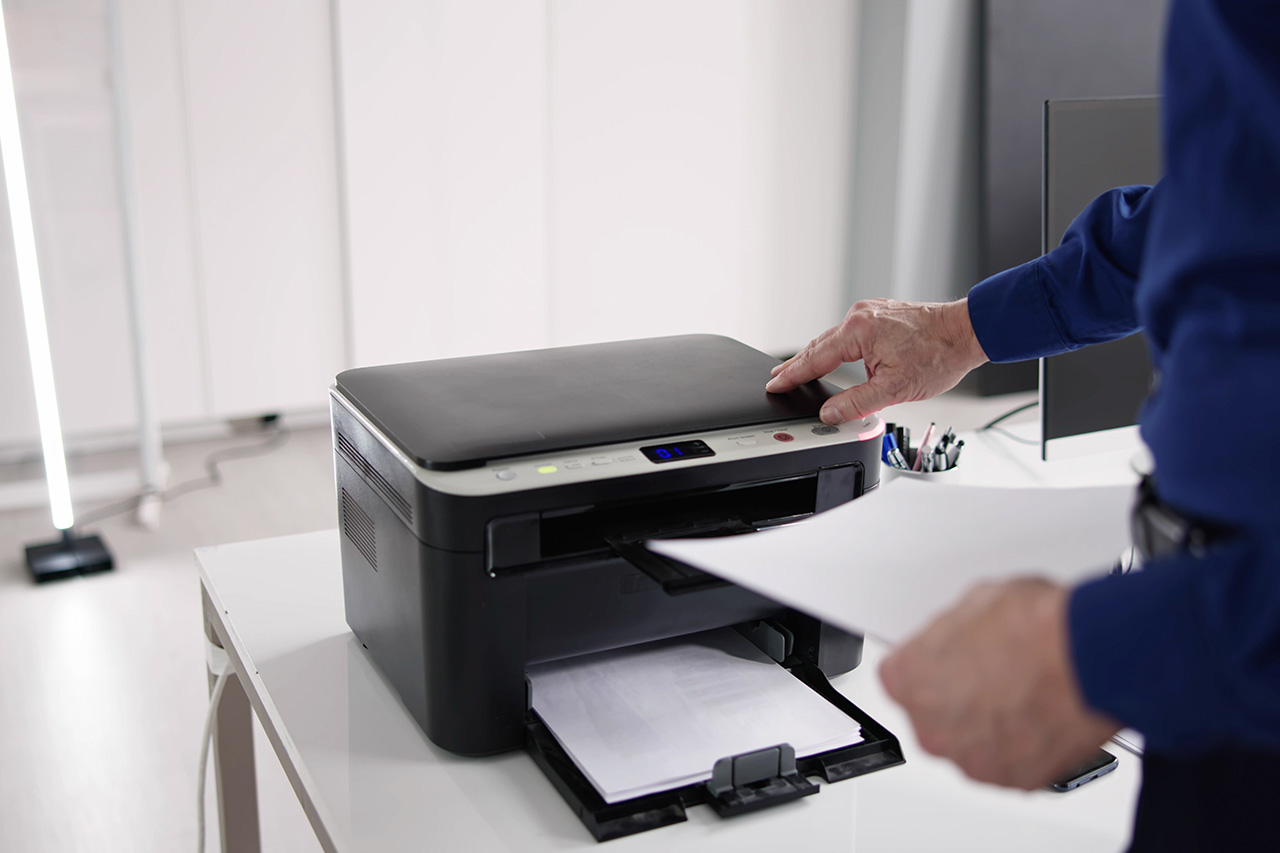 Mężczyzna obsługuje drukarkę i wkłada kartkę papieru. - zdjęcie