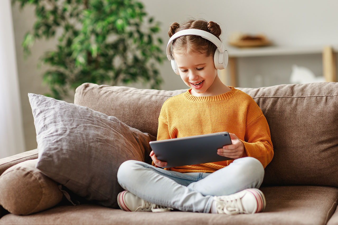 Dziewczynka siedzi na kanapie, uśmiechając się, trzymając tablet w rękach. - zdjęcie
