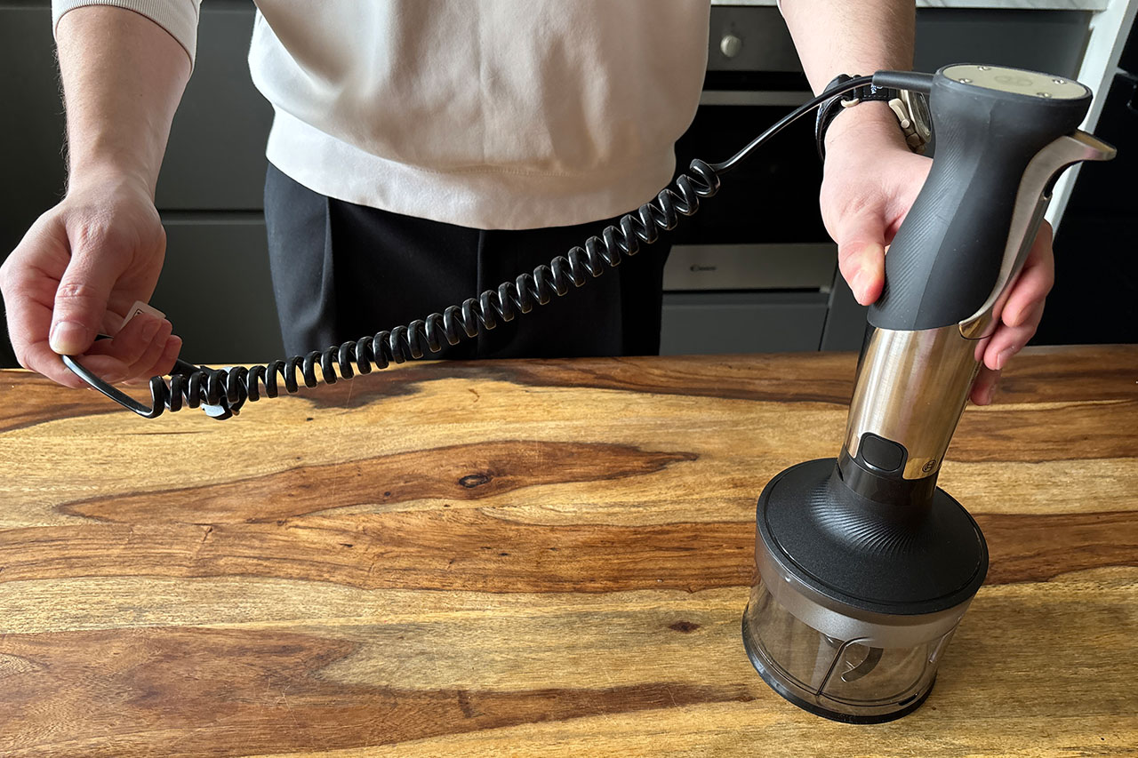 Dłoń trzyma blender Bosch Ergomaster z pojemnikiem i spiralnym rozciągliwym kablem. - zdjęcie